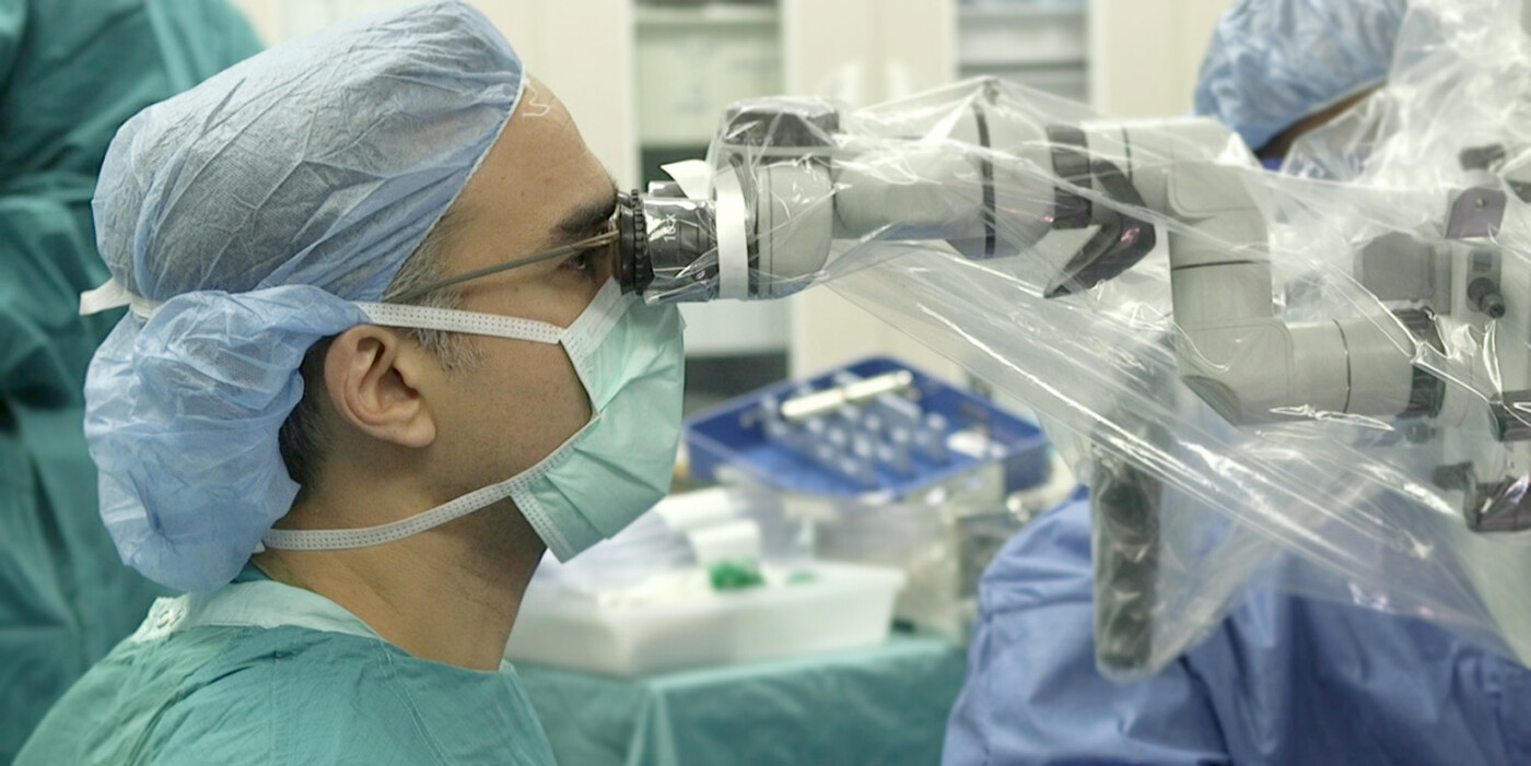 A doctor looks through a microscope during surgery.
