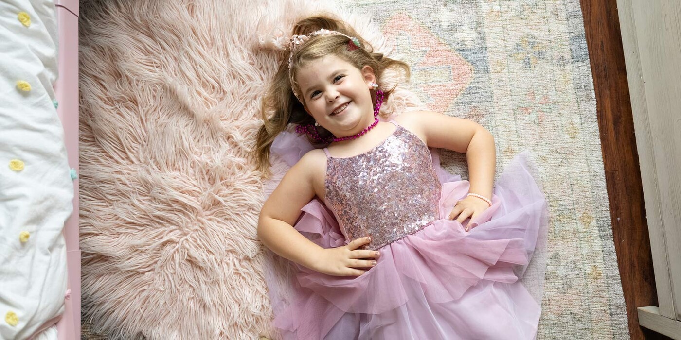 Camden Fisher, dressed in pink and sparkles, lays on the floor smiling up at the camera