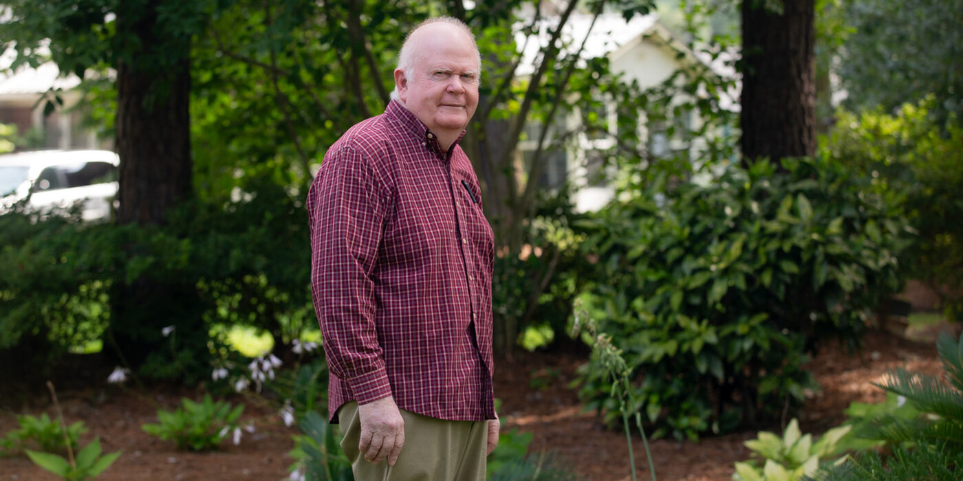 David Phillips stands in front of some trees and other vegetation