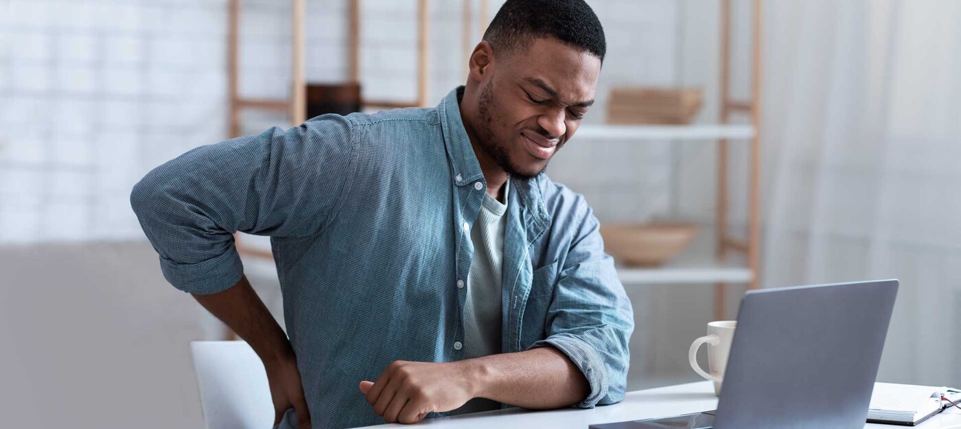 A man holds his back in pain while sitting in front of a computer