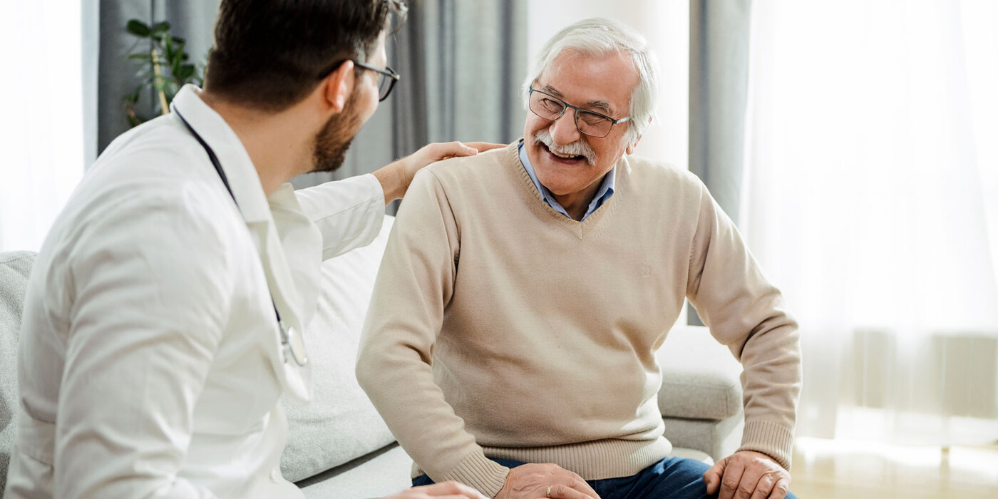 A doctor puts his hand on a patient's shoulder who smiles in clinic
