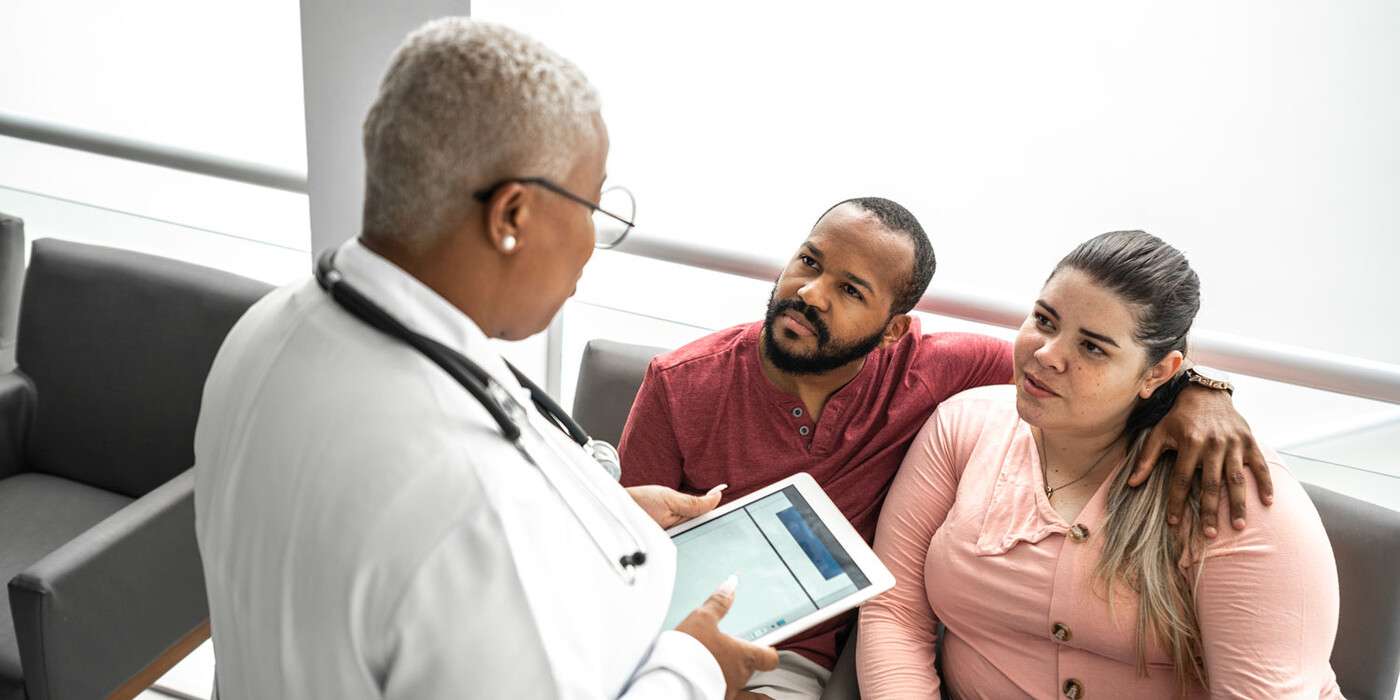 A doctor speaks with a couple who sit in a waiting or consult area