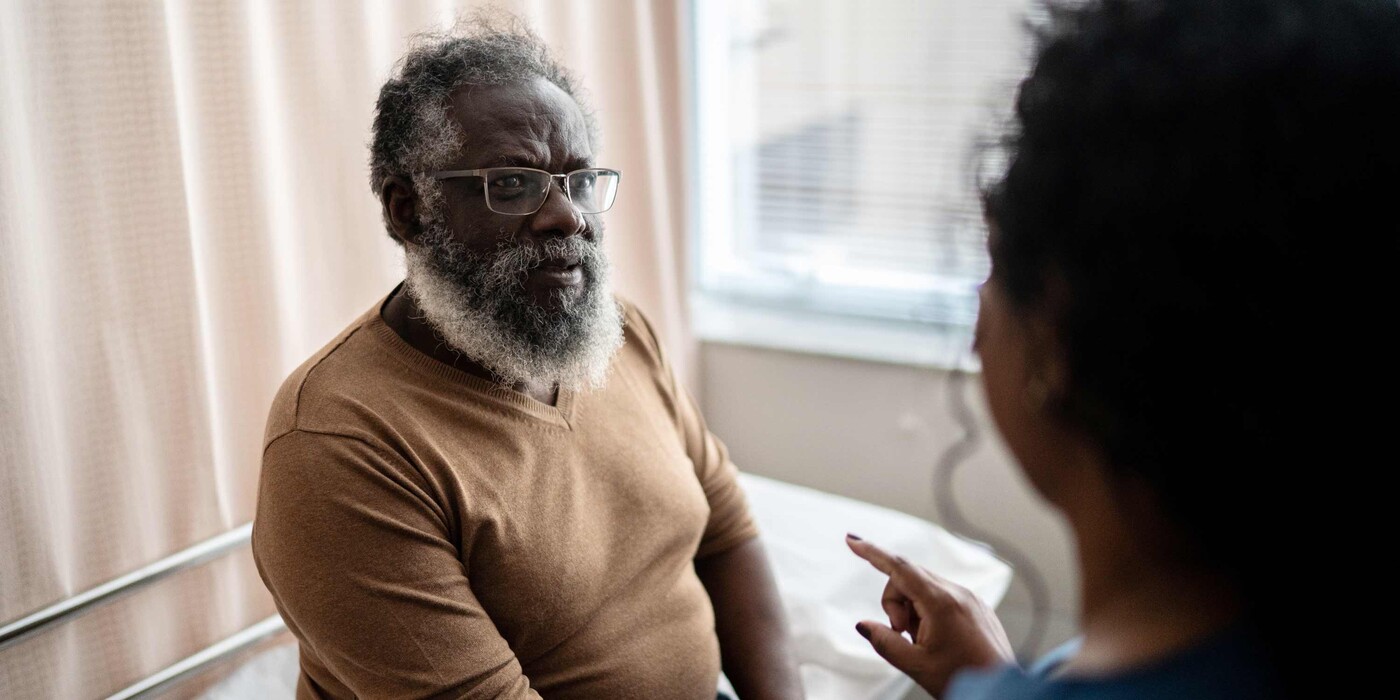 A patient sits on a hospital bed and listens to a provider