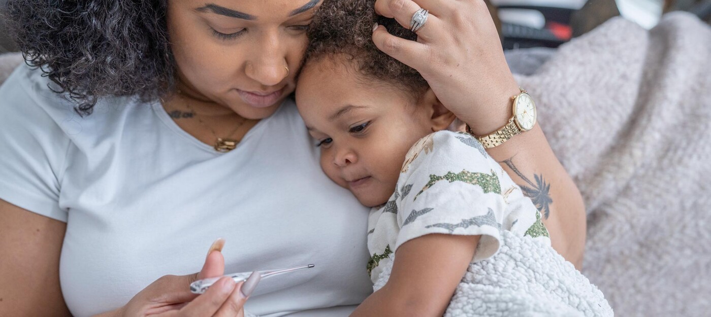 A mom comforts her young son while looking at a thermometer together