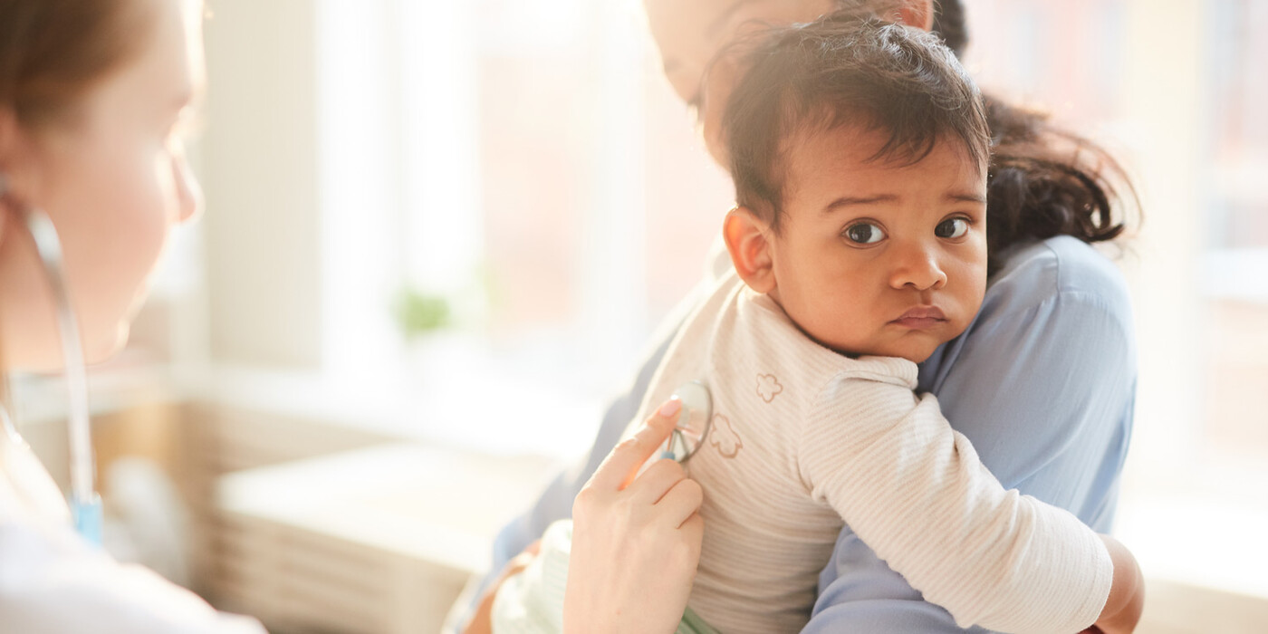 A doctor listens to a young boys breathing with a stethoscope. The boy is being held by his mother.