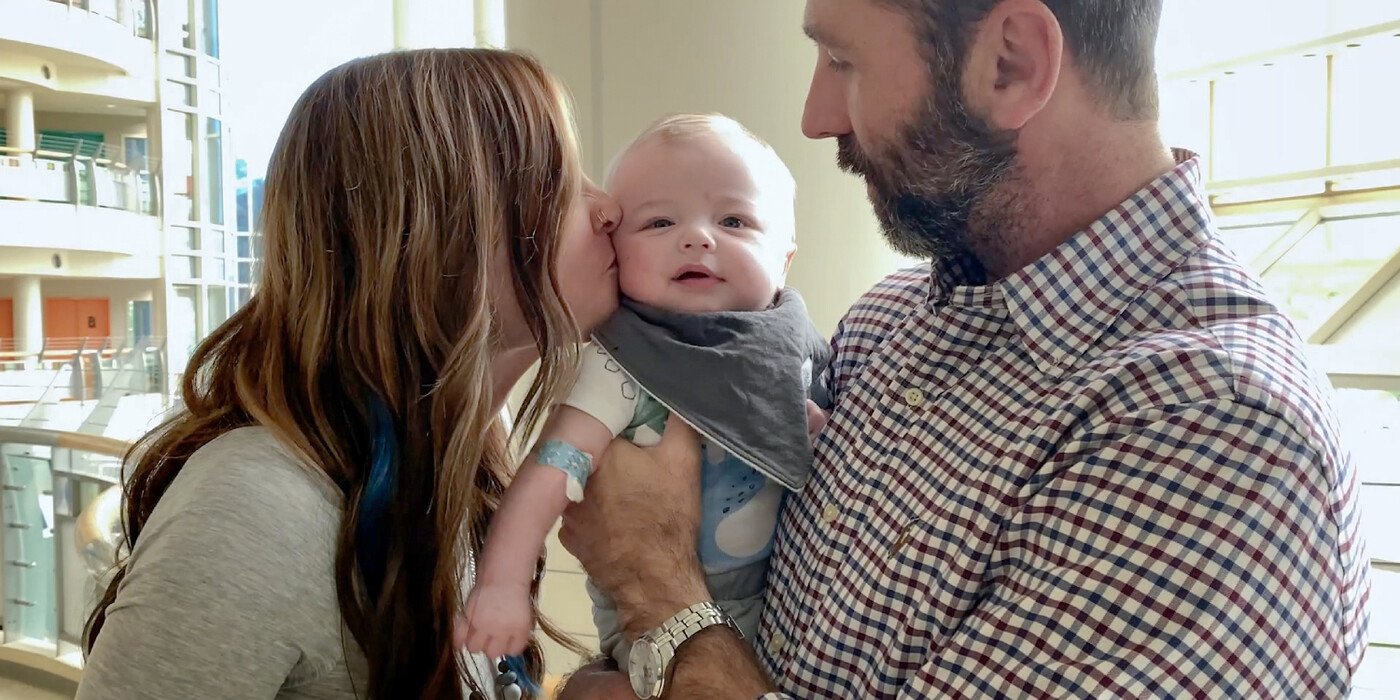 Drew Hobby holds his son Asher, while Asher's mother Kayle kisses Asher on the cheek.