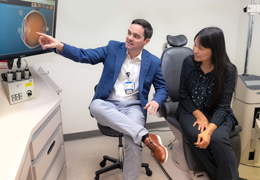 A doctor points to a cataract model on a computer screen as a patient looks on