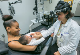 A provider does an eye exam on a young patient who is being held by their guardian