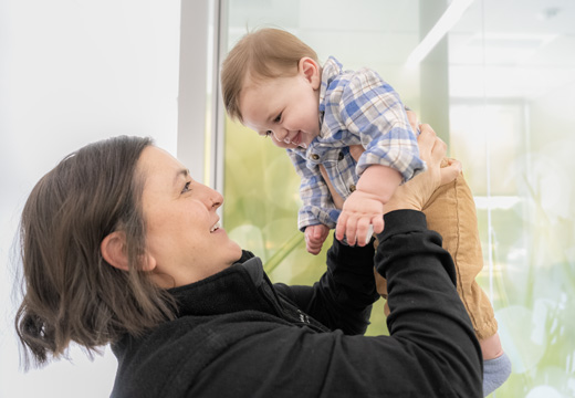 A provider smiles as she holds up a baby playfully in the air