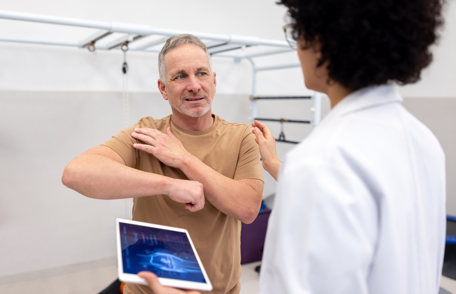 A man touches his shoulder in discomfort as a doctor goes over imaging with him