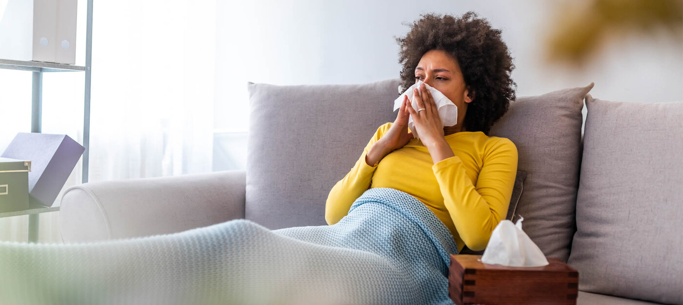 A woman sits on a cough and wipes her nose with a tissue.